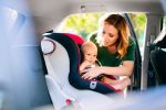 Young mother putting baby in the car seat.